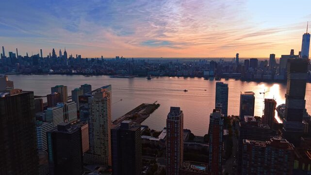 Manhattan skyscrapers extend across the Hudson beyond Jersey City rooftops. Warm light reflects on the right side of the river below streaked clouds and a pink horizon.