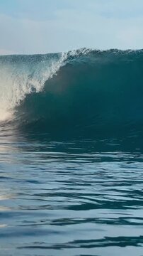 Close up view of clean ocean surfing wave barrel curling with white foam in clear blue sea. Perfect background for surfing, water sports, and extreme adventure. Vertical video