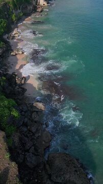 Sunshine illuminates crashing waves. Golden sunlight dances across turbulent ocean. Bright sunlight highlights frothy surf pounding rugged coastal formations and sandy coves, vertical video