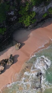 Quiet coastal paradise. Hidden seaside cove with sandy shores. Remote rocky shore featuring soft pink sands. Secluded cliff edge beach with peachcolored grains and calm waves, vertical video