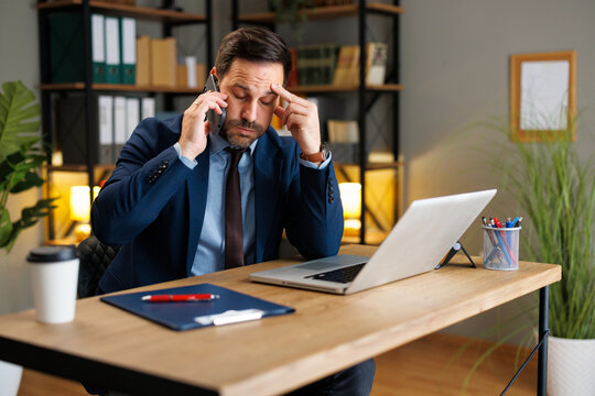Stressed businessman taking a phone call while working at a laptop