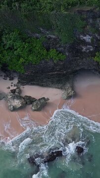 Quiet coastal paradise. Hidden seaside cove with sandy shores. Remote rocky shore featuring soft pink sands. Secluded cliff edge beach with peachcolored grains and calm waves, vertical video