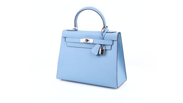 Seamless 360 degree rotation of a light blue handbag in 4K studio footage, revealing its trapezoid shape, top handle, textured finish and silver clasp on white.