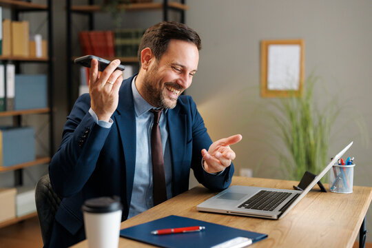 Businessman laughing during a smartphone call at his office desk