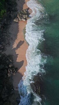 Sunshine illuminates crashing waves. Golden sunlight dances across turbulent ocean. Bright sunlight highlights frothy surf pounding rugged coastal formations and sandy coves, vertical video