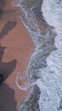 Shimmering emerald seascape with vibrant plant life surrounding rugged shoreline. Bright green waters swirl vigorously around jagged rocks amid abundant plant coverage, vertical video of Bali coast