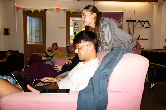 Young man working on a laptop while a friend leans in