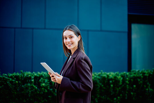 Businesswoman holding a tablet outside a modern office, smiling confidently and conveying professionalism, leadership, and corporate success