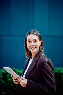 Businesswoman holding a tablet and smiling outdoors, conveying confidence, digital expertise, and a modern professional approach