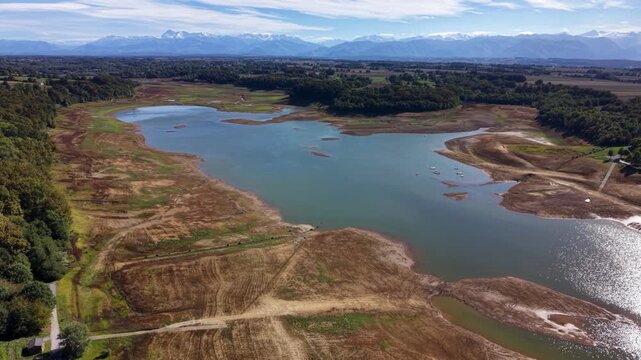 Aerial camera pans right over a dried lake, exposing its shore and water in France during daytime