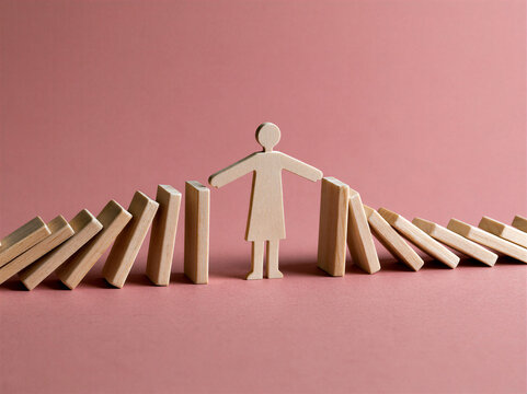 Cutout wooden figure of a business woman with her arms outstretched stopping wooden dominos falling on her from both sides