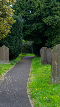 A wide paved path running through an old church cemetery, surrounded by tall green trees