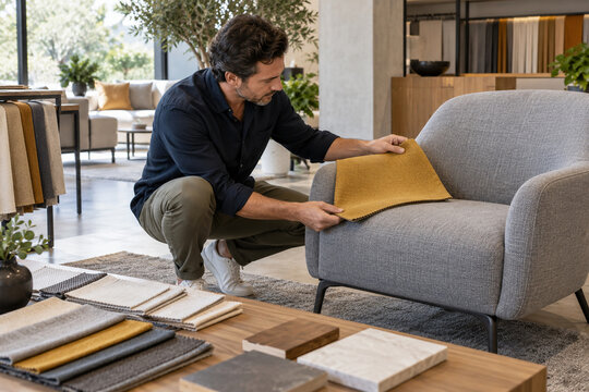 Man compares a mustard fabric swatch against a gray sofa in a modern furniture showroom