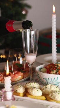 Close-up of sparkling amber-colored wine being poured into a champagne flute on a festive Christmas dinner table. Traditional Italian holiday appetizers, including smoked salmon sandwiches, grilled po
