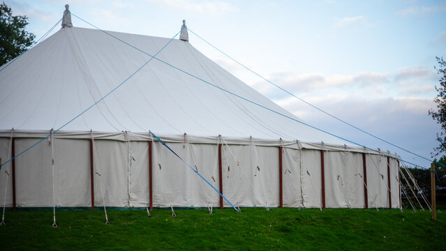 A traditional white canvas tent (marquee) on poles, with red wooden posts and white side walls, set up on a green lawn
