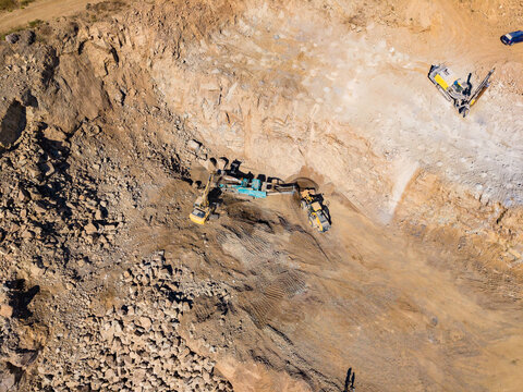 Excavators dig and move rock across a quarry floor in an overhead view of an active work site