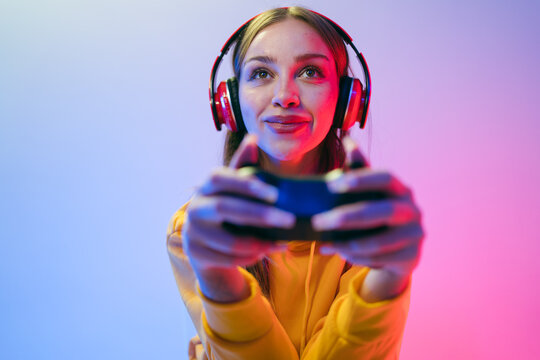 Young woman wearing headphones holds a game controller in colorful studio lighting