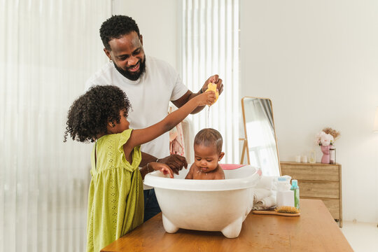 Father and daughter gently bathe a baby in a tub at home