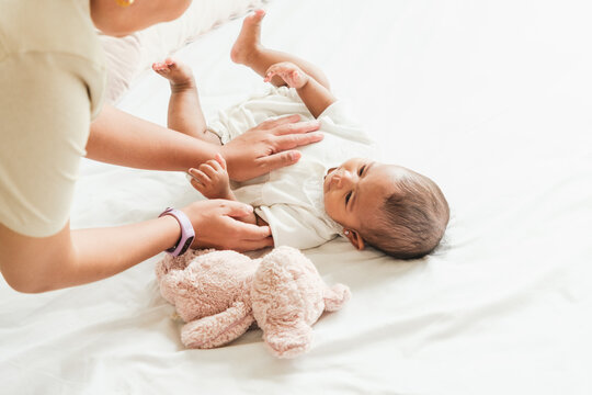 Caregiver gently plays with a smiling baby lying on a bright bed