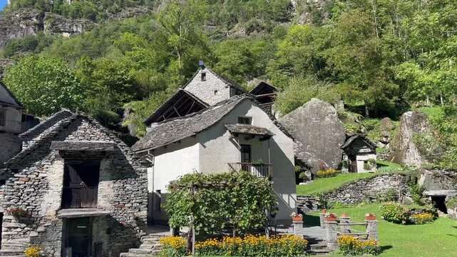 Traditional stone house and lush garden surrounded by trees and rocks in Roseto, Switzerland, scenic rural alpine village landscape on a sunny day