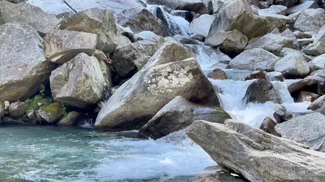 Mountain stream cascading through massive granite boulders with clear turquoise water in Foroglio, Switzerland, scenic alpine nature landscape