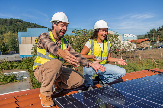 Multicultural solar engineers installing renewable energy panels laughing on rooftop