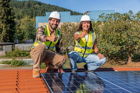 Multicultural engineers installing solar panels on rooftop giving thumbs up