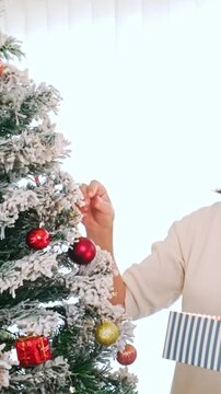 Person decorates a snow flocked Christmas tree with a red bauble indoors
