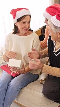 Woman opens a Christmas present with an older couple seated together at home