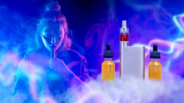 Electronic cigarette vaping. Young woman inhales vapor from a vape device beside e-liquid bottles and a vaping mod under colorful neon lighting.
