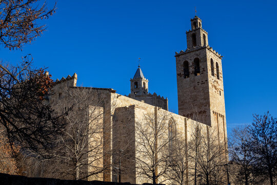 Romanesque bell tower and tiled spire of the Monestir de Sant Cugat, a medieval Benedictine monastery, against a deep blue sky in Catalonia