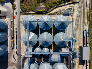 Aerial view of grain storage silos beside a road and railway tracks at an industrial facility during daytime © DSMT
