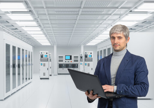 Data center operations, IT specialist uses a laptop to monitor server racks, network equipment and automated systems inside a modern technical facility.