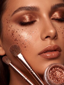 Close up portrait featuring a woman with shimmering makeup and cosmetic brushes beauty glitter bronze complexion face