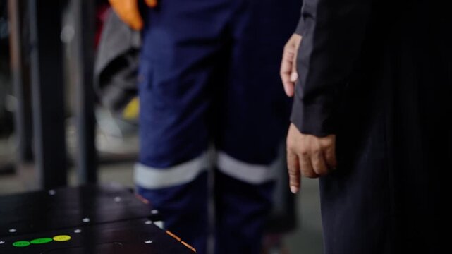A bearded technician with a tablet talking to a woman customer, then a close view of black lithium battery modules with green and yellow status dots as hands point