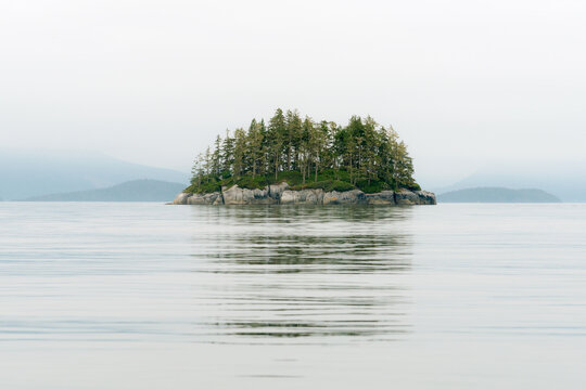 Canada, BC, Broughton Archipelago.  A single small island on a foggy morning in the calm waters of the Queen Charlotte Strait