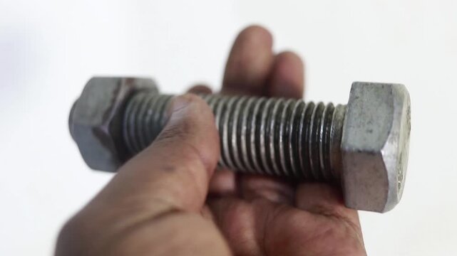 Industrial worker holding large metallic threaded bolt and nut in workshop environment securely