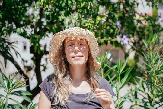 Freckled European Female in Her 40s Closing Her Eyes as Straw Hat Casts Lace Shadows on Her Face in Harsh Summer Sun