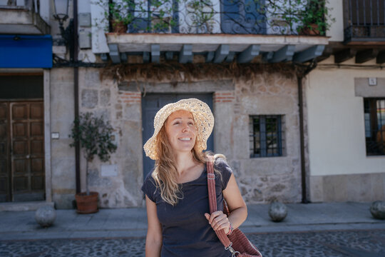 Relaxed European Female in Her 40s Wearing Straw Hat on Sunlit Cobblestone Street in Historic Spanish Town