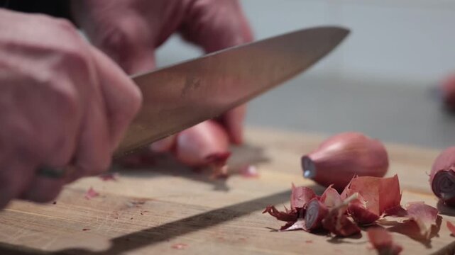 Stockholm, Sweden A cook cuts and peels shallots or onions on a wooden board with a large knife. 
