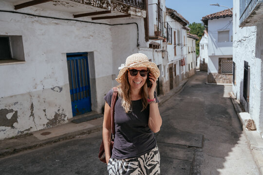 Smiling middle aged woman talking on smartphone while walking through Spanish village