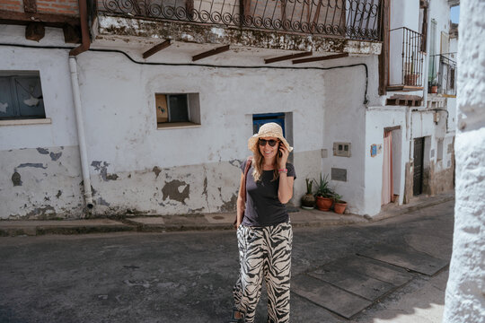 Happy middle aged woman making phone call on quiet street in small Spanish village