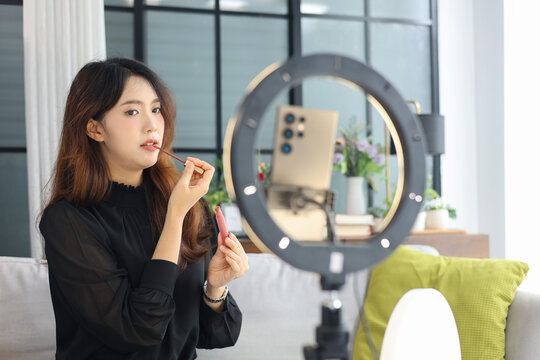 Young Asian influencer filming a beauty makeup tutorial video at home.