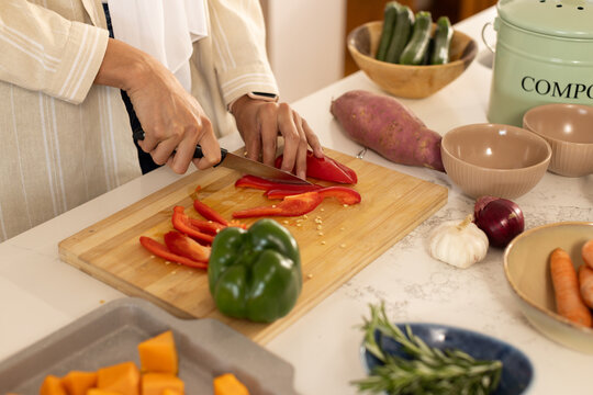 African American woman in striped shirt slicing red bell pepper using chef's knife on home counter