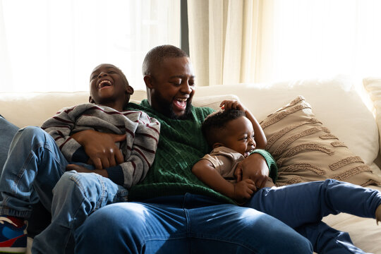African father with two sons laughing cuddling on sofa at home with textured pillows