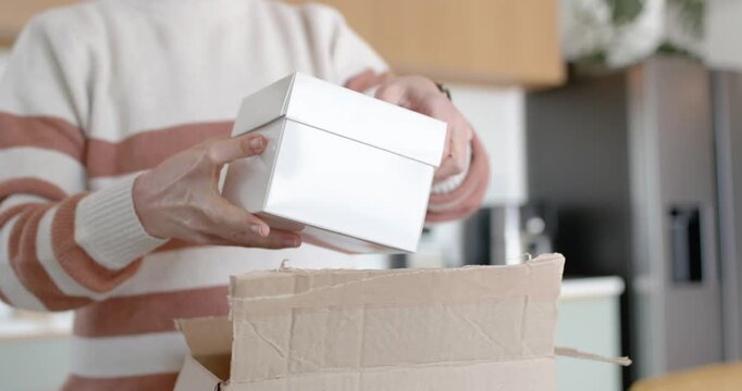 Woman at kitchen countertop unboxing shipped box, lifting white gift box, checking contents
