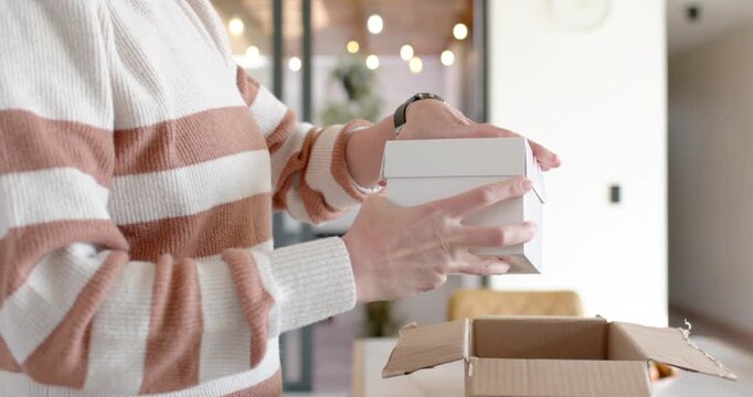 After opening corrugated box, woman unpacking small white gift box and checking contents at table