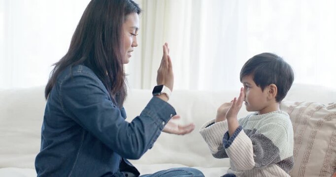 Diverse woman and child on sofa, woman holding child's hands, raising palms, clapping
