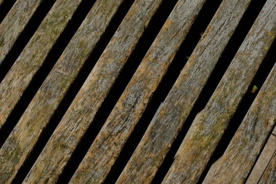 Weathered gray wooden bench slats with moss and cracks, diagonal rustic wood texture