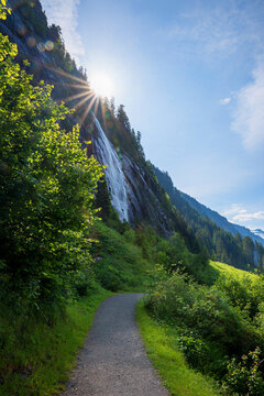 idyllic trail Wasserfallweg, sunburst behind waterfall and rock face. Landscape Stillup valley